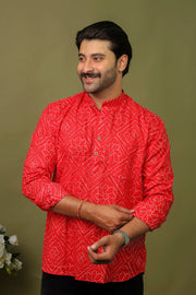 Man wearing a red Bandhani printed kurta shirt with black jeans against an olive green background.